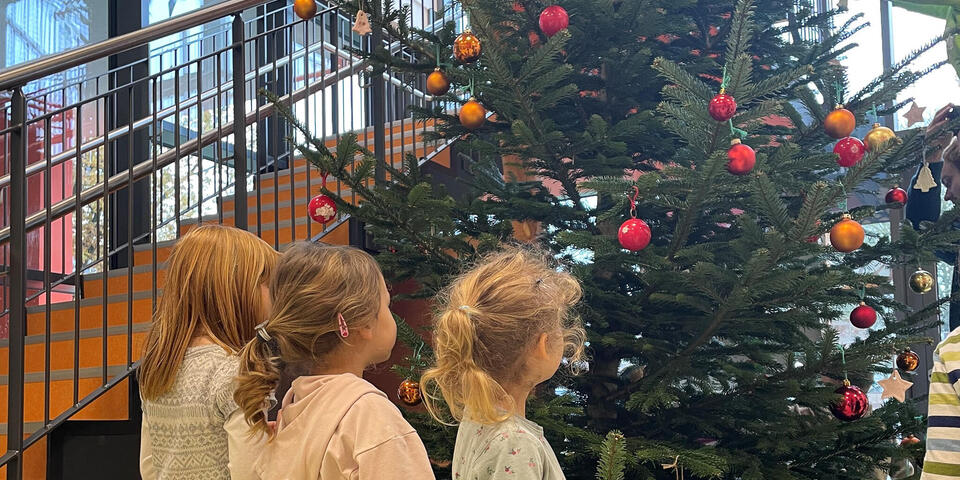 Drei kleine Mädchen stehen vor einem geschmückten Weihnachtsbaum