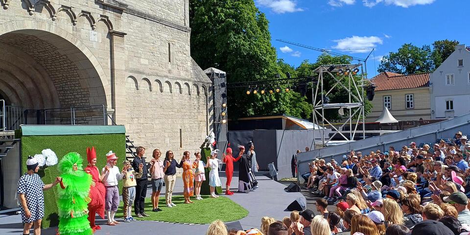 Ein Bühne mit Darstellern. Davor Zuschauer.