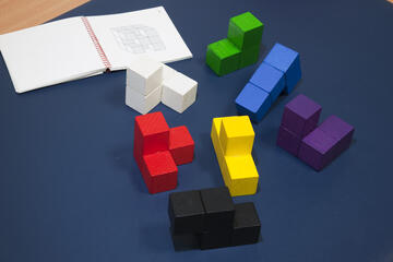 Detailaufnahme bunte Bauklötze und ein Notizbuch auf einer dunkelblauen Schreibunterlage.