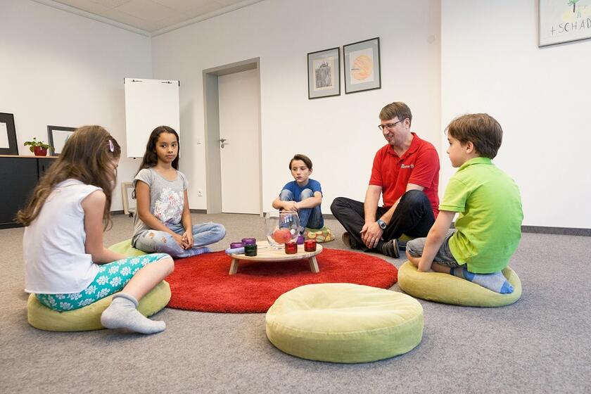 Trauernde Kinder sitzen mit einem Trauerbegleiter im Kreis um eine Kerze.