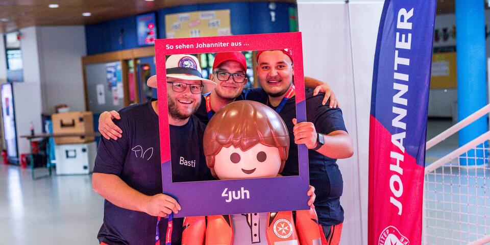 Drei Johanniter halten einen Johanniter Fotorahmen vor sich und eine Johanniter Playmobil-Figur und posieren für ein Foto.