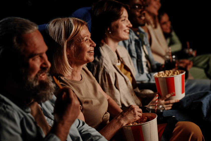 Mehrere Menschen sitzen lachend im Kino und essen Popcorn.