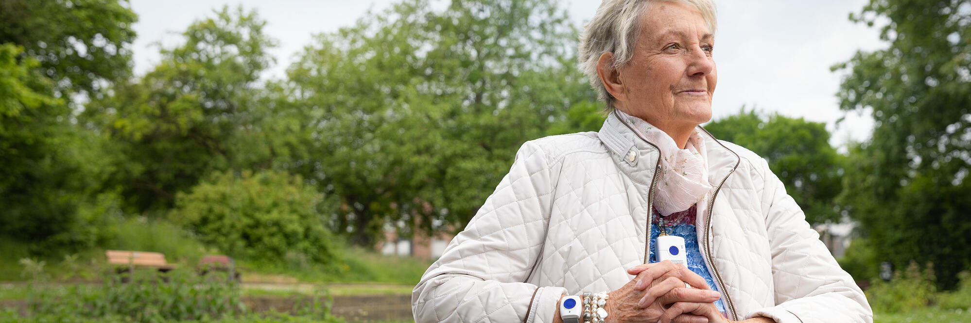 Frau mit Hausnotruf-Gerät schaut in die Natur.