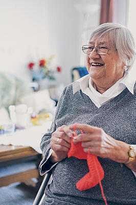 Eine Seniorin in grauem Pullover strickt