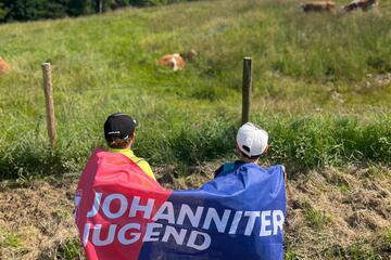 Jugendliche mit einer Johanniter-Jugend-Fahne auf dem Rücken schauen in Richtung Berge