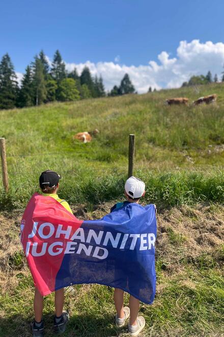 Jugendliche mit einer Johanniter-Jugend-Fahne auf dem Rücken schauen in Richtung Berge