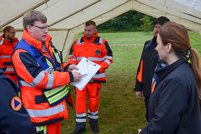 Tim Carstensen, Ehrenamtlicher bei den Johannitern aus Lübeck, erläutert Innenministerin Magdalena Finke die Transportorganisation.