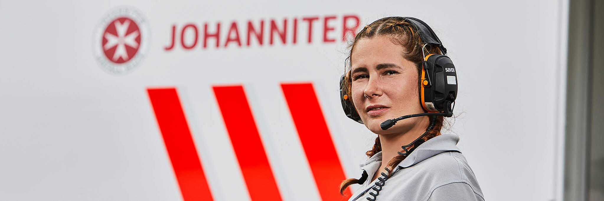 Mitarbeiterin mit Köpfhörern vor einem Johanniter-Einsatzwagen