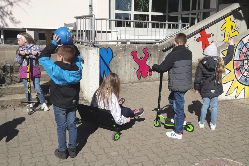 Kinder beim Rollerfahren im Schulhof