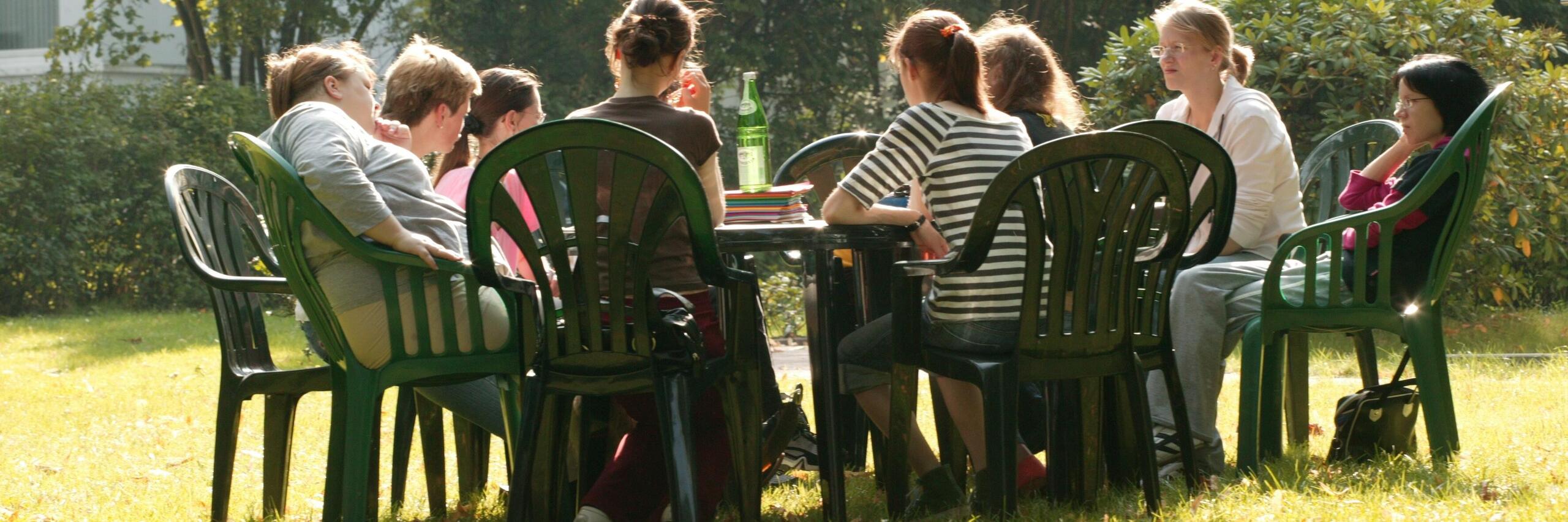 Gruppe Jugendlicher und junger Erwachsener sitzen an einem Tisch im Garten der Klinik am Korso