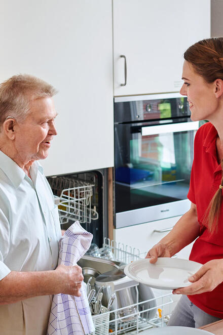 Eine junge Frau hilft einem älteren Mann beim Geschirrabtrocknen