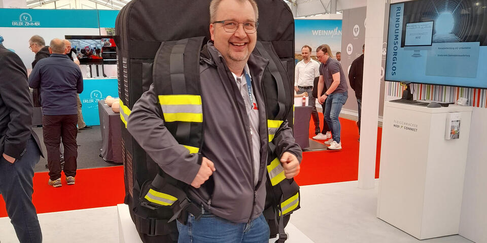 Ein Mann probiert auf einer Messe eine riesigen Rettungsrucksack an
