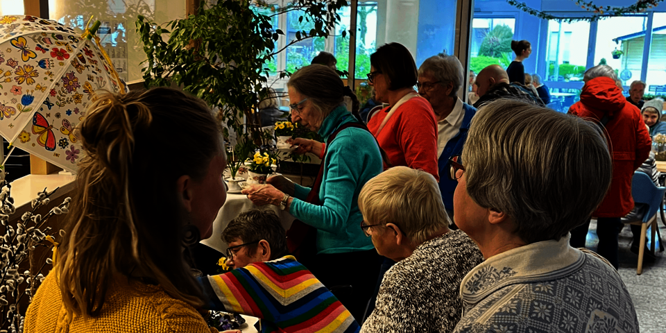 Gruppe von Besucher*innen an Ständen, mehrere Personen betrachten Pflanzen und Handarbeiten.