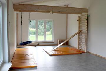 Orangefarbene Matten auf dem Boden, in den Ecken findet man eine Vogelnestschaukel und eine Sprossenleiter.