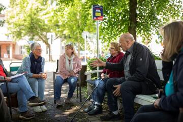 Menschen auf Plauderbank und Plauderplatz-Zusatzstühlen im Gespräch