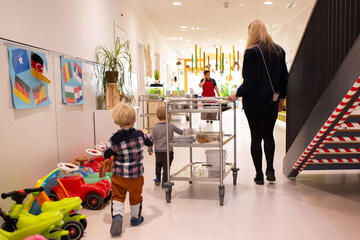 Eine Erzieherin fährt den Essenswagen mit Mittagessen durch die Kita