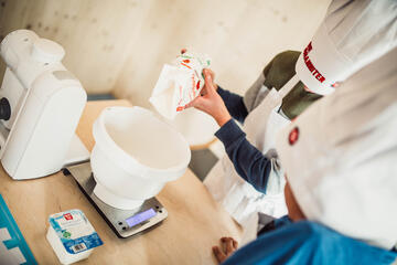 Kinder mit Kochmützen wiegen Zutaten auf einer Küchenwaage.