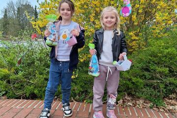 Zwei Mädchen halten ihre Osterschätze in beiden Händen: eine Naschitüte und ein Osterkörbchen