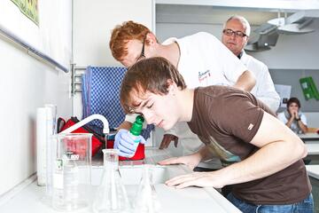 Ein Junge hält seinen Kopf über ein Waschbecken. Ein Schulsanitäter unterstützt ihn beim Augenspülen.