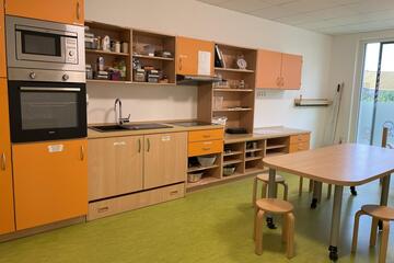 Eine Kinderküche mit Ofen, Mikrowelle, Herd, Spüle sowie Geschirr, einem Esstisch mit kleinen Stühlen und Zutaten zum Kochen.