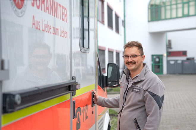 Ein Johanniter ist dabei die Tür zu einem Johanniter Einsatzfahrzeugs zu öffnen.