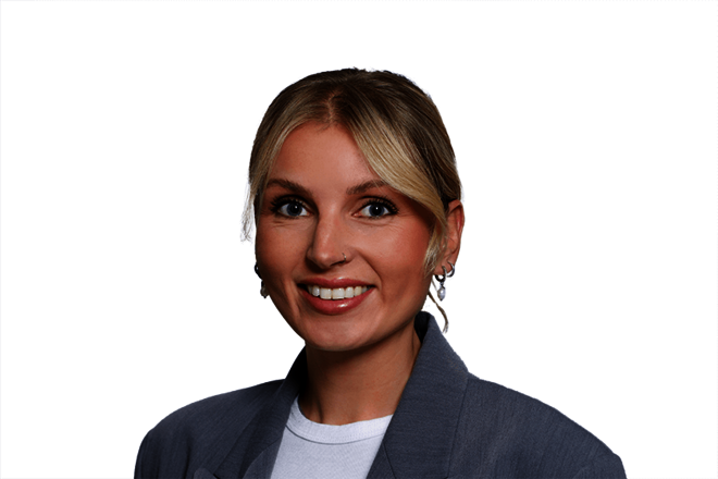 Porträt einer lächelnden Frau mit blondem Haar, Creolen und grauem Blazer vor weißem Hintergrund.