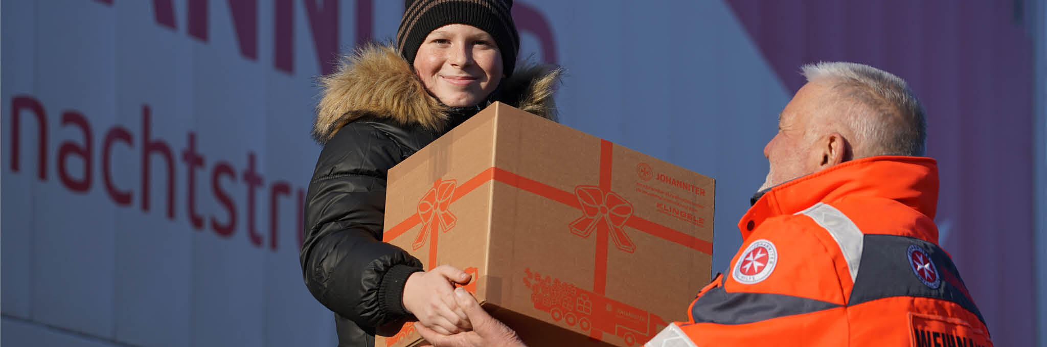 Ein Mitarbeiter der Johanniter überreicht einem kleinen Jungen ein Weihnachtspaket