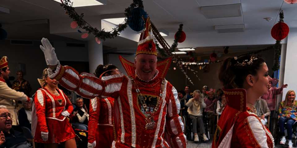 Karnevalsprinzen in rot-weißen Uniformen ziehen durch den Raum, das Publikum applaudiert.