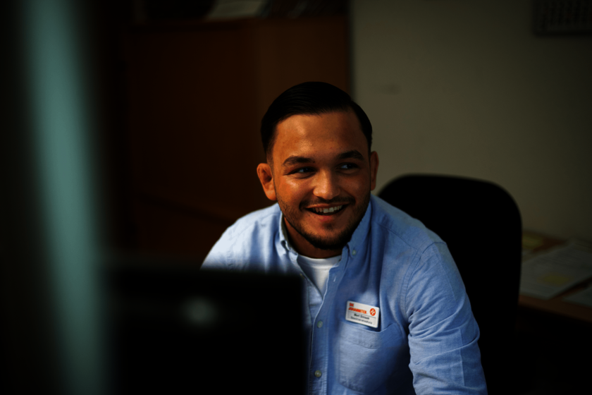 Ein Mann in hellblauem Hemd sitzt am Schreibtisch und lächelt zur Seite