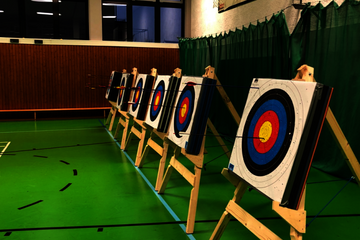 6 Bogenschießstände in einer Sporthalle mit grünem Boden.