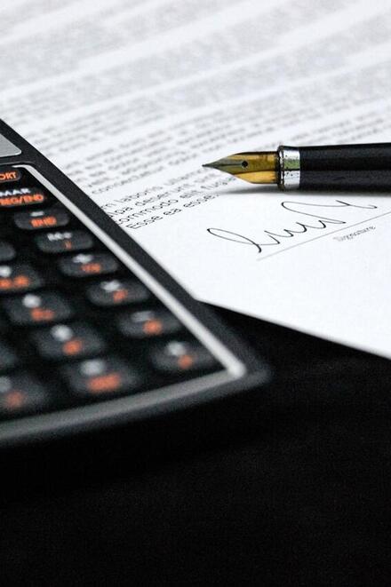 Taschenrechner und Füllfederhalter liegen auf einem unterschriebenen Dokument.
