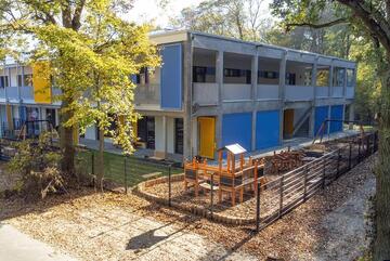 Ein Panorama der Außenansicht der Kita Lumi Natura mit Schaukeln und Spielplattformen.