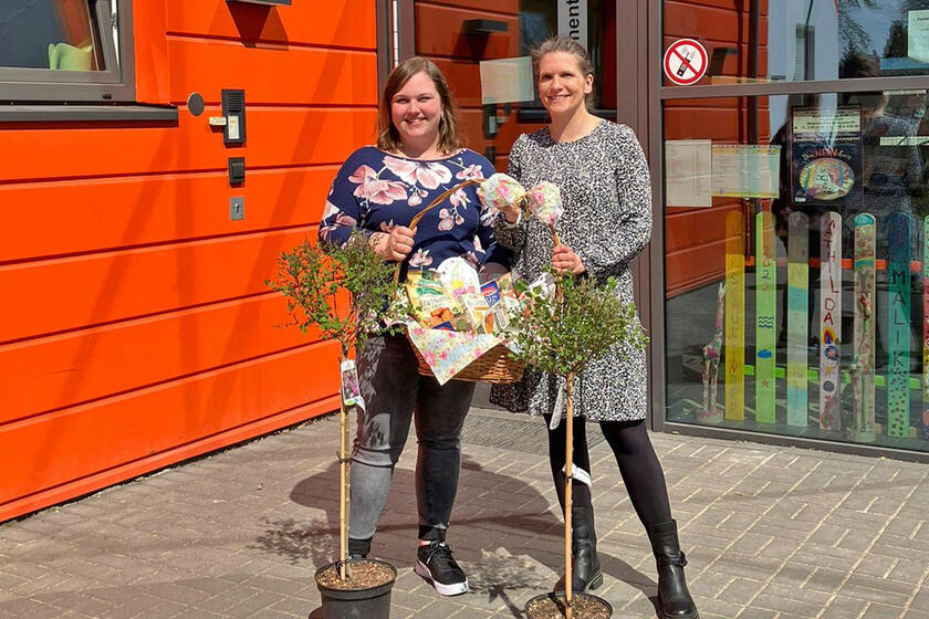 Zwei Frauen mit Geschenkkorb und zwei kleinen Bäumchen vor der Kita