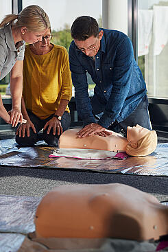 Ein Mann reanimiert eine Puppe und wird von einer Johanniter-Dozentin angeleitet.