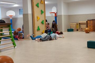 Blick in den Bewegungsraum mit Sportgeräten, Bällen und turnenden Kindern.
