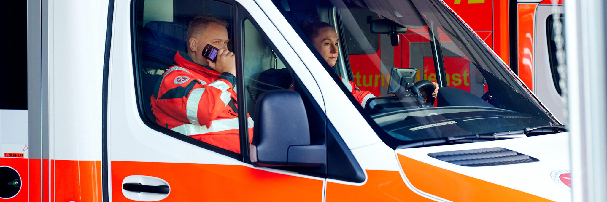 Zwei Johanniter sitzen in einem Rettungswagen und verlassen die Rettungswache
