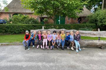 Die Kinder sitzen aufgereiht vor einem Reetdachhaus