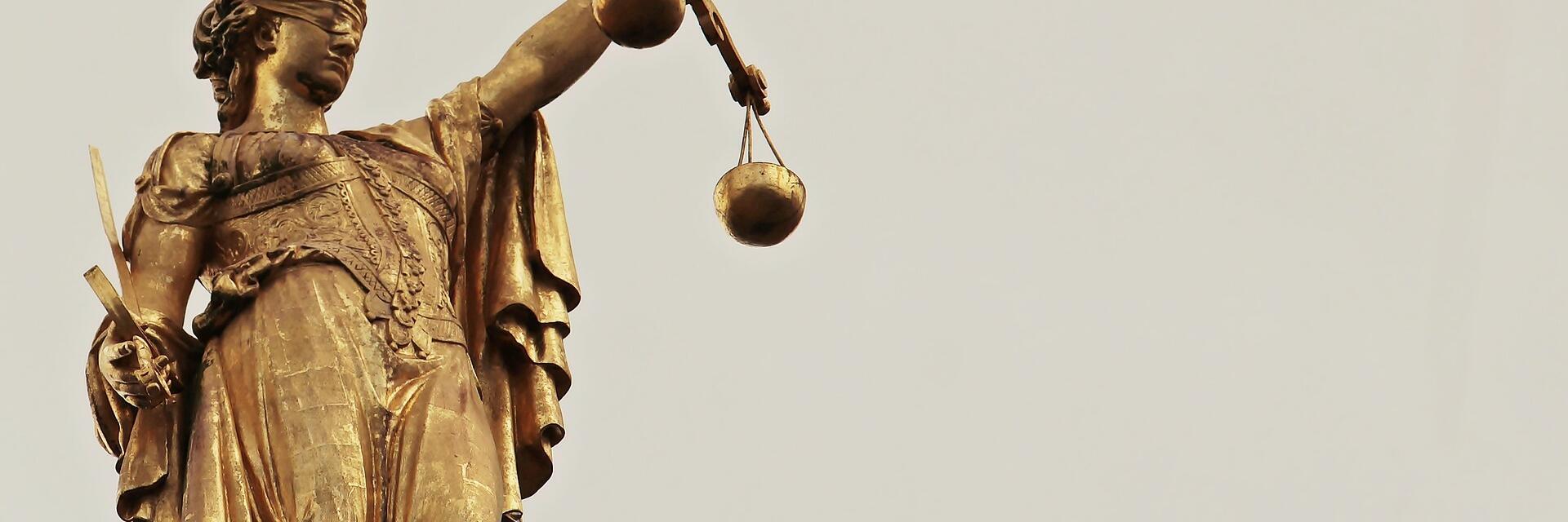 Goldene Statue der Justitia mit Augenbinde, Schwert und Waage als Symbol für Gerechtigkeit.