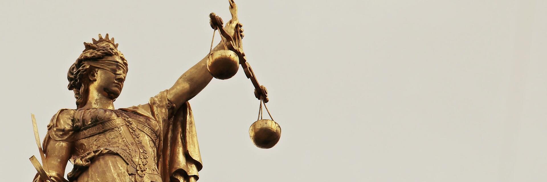 Goldene Statue der Justitia mit Augenbinde, Schwert und Waage als Symbol für Gerechtigkeit.