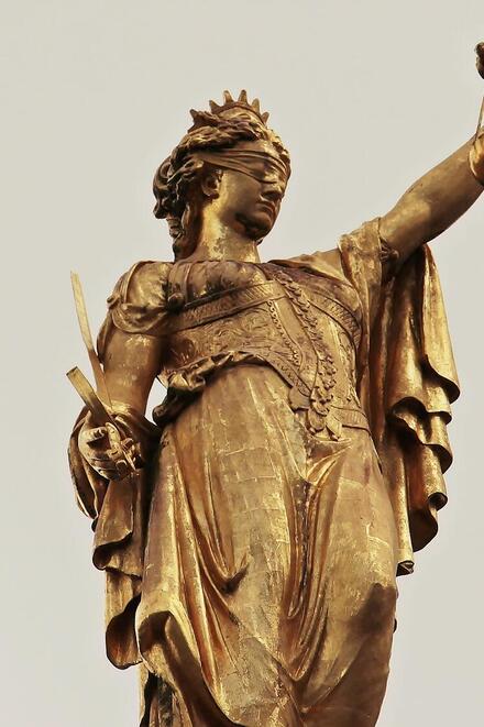 Goldene Statue der Justitia mit Augenbinde, Schwert und Waage als Symbol für Gerechtigkeit.