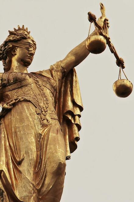 Goldene Statue der Justitia mit Augenbinde, Schwert und Waage als Symbol für Gerechtigkeit.
