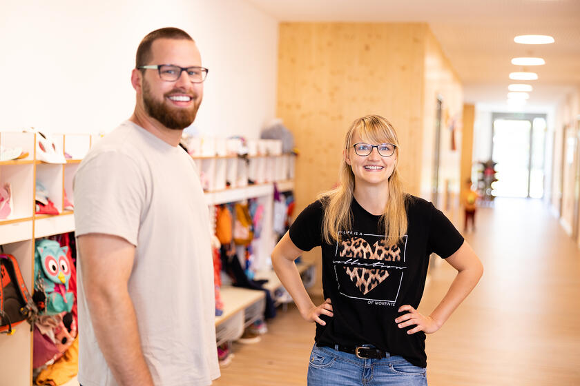 Zwei lächelnde Erzieher stehen in hellem Flur mit Garderobenfächern.