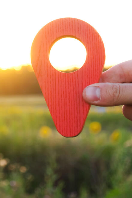 Eine Hand hält eine Standortmarkierung hoch, im Hintzergrund ist eine Blumenwiese zu sehen