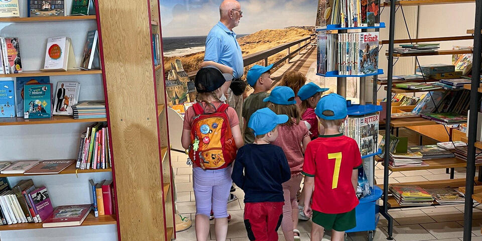 Kinder folgen einem Mann durch eine Bücherei