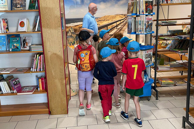 Kinder folgen einem Mann durch eine Bücherei