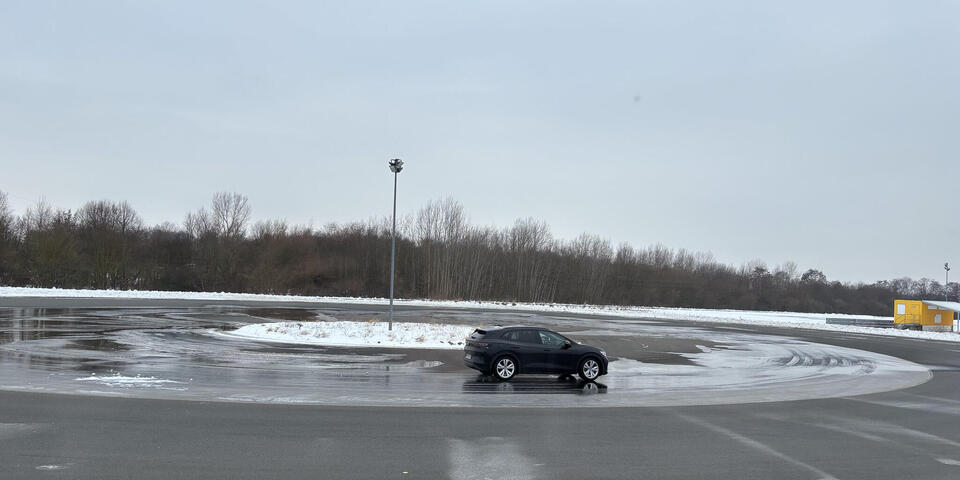 Ein schwarzes Auto fährt auf nasser Fahrbahn Kurven.