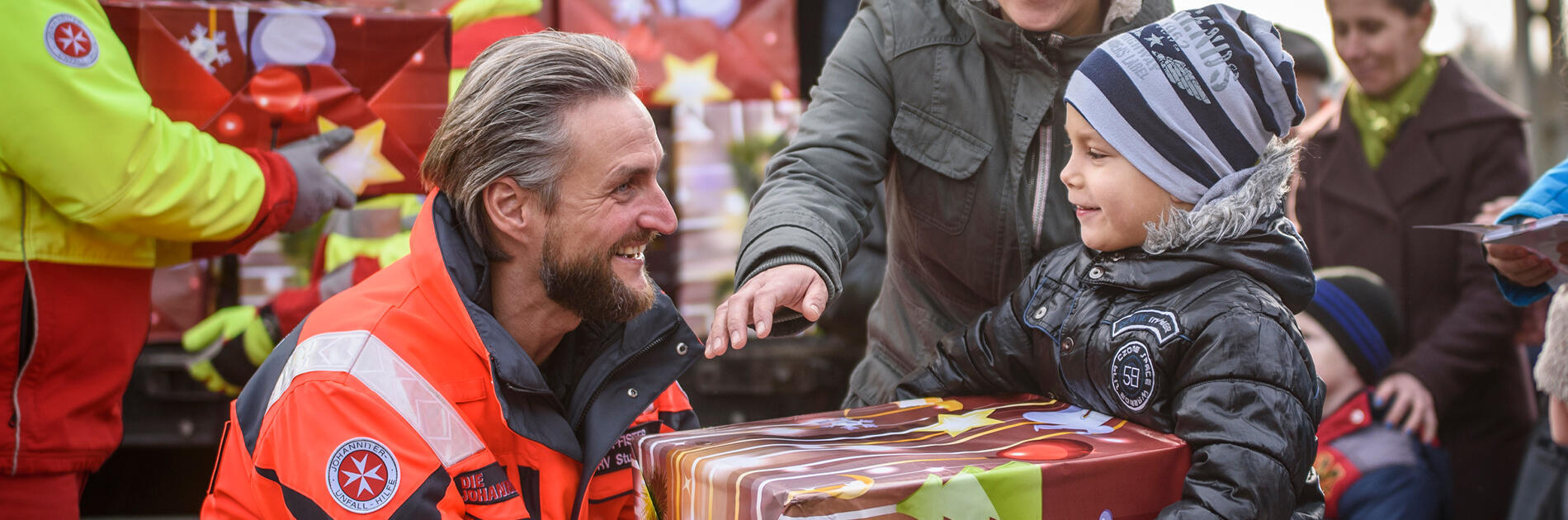 Ein Mitarbeiter der Johanniter überreicht einem kleinen Jungen ein Paket