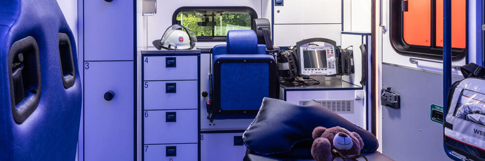Das Innere eines Rettungswagens zeigt eine Patiententrage mit einem kleinen Teddybären drauf.