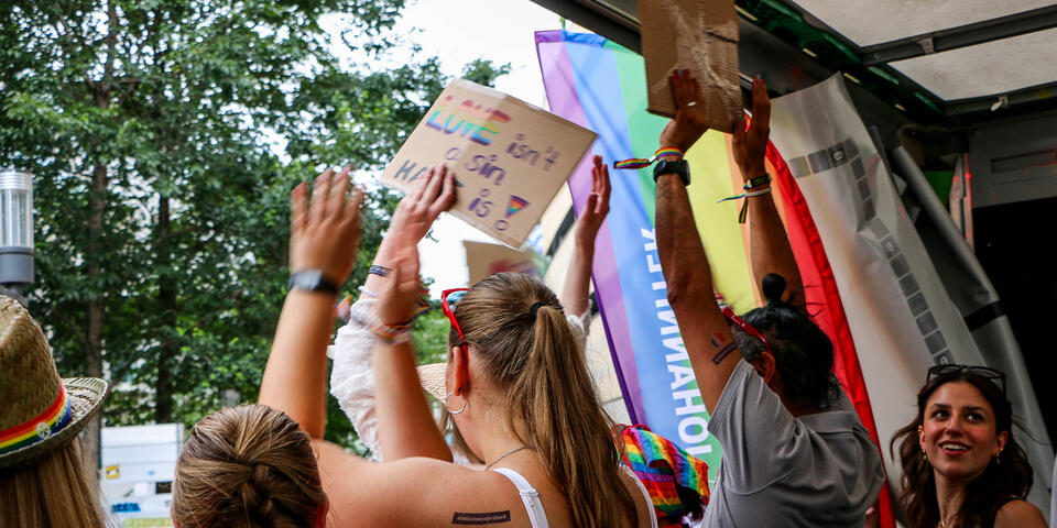 Mehrere feiernde Personen auf einem Festwagen, die die Hände in die Luft strecken und bunte Plakate hochhalten.