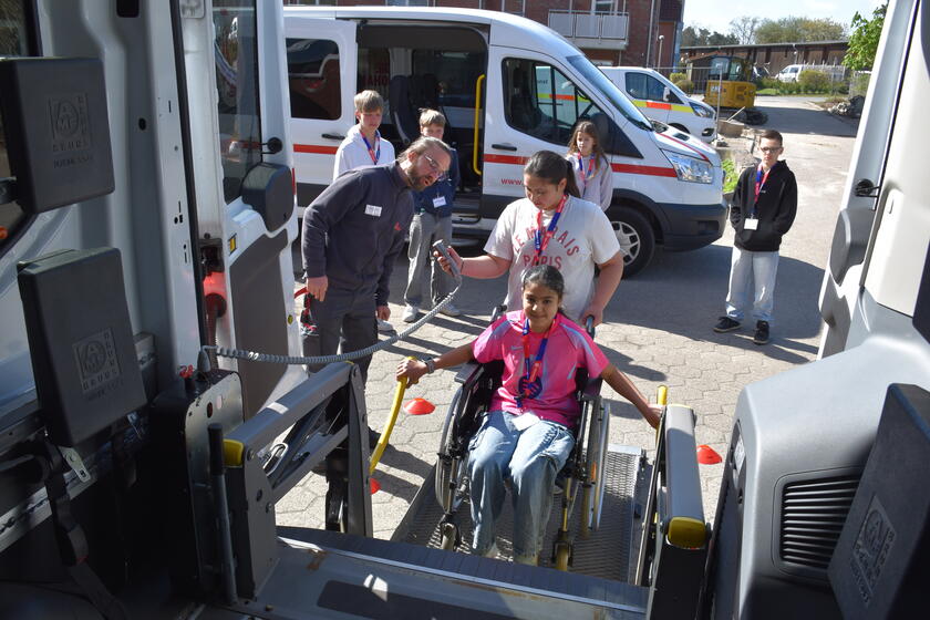 Einigen Schülerinnen und Schüler wird der Bus des Johanniter-Fahrdienstes erklärt und sie dürfen selbst einmal im Rollstuhl mitfahren
